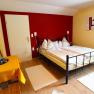 Gem&uuml;tliches Schlafzimmer mit Doppelbett, Tisch und St&uuml;hlen, gelben W&auml;nden und rotem Vorhang.