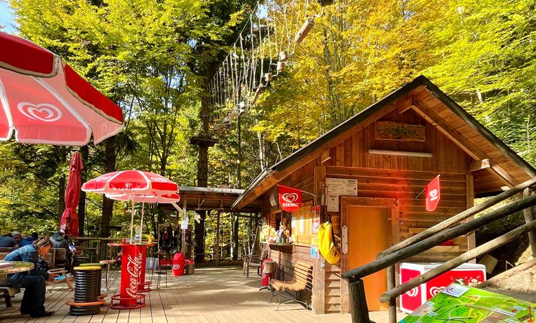 Holzhütte mit Sonnenschirmen und Kletterpark im Hintergrund.