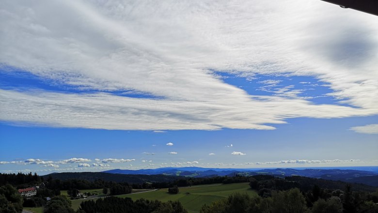 Landschaft mit Hügeln, Wäldern und weitem Himmel mit Wolken.