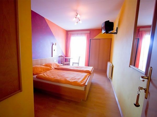 Ein gemütliches Gästezimmer mit Doppelbett, bunten Wänden und einem kleinen Fernseher an der Wand.