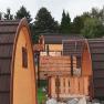Several wooden glamping huts with brown roofs in a wooded area.