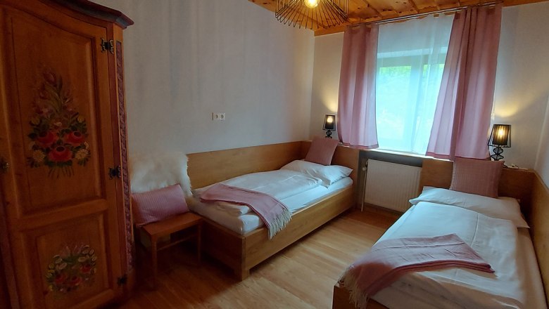 Cozy bedroom with two single beds, wooden furniture and pink curtains.