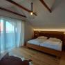 A cozy double room with a wooden floor, a large bed, curtains and a small table. A lamp hangs from the ceiling.