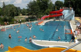 Ein Freibad mit Wasserrutsche und spielenden Menschen.