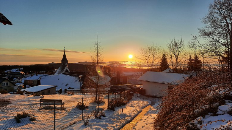 Winter sunrise over a snowy landscape with a church and houses.