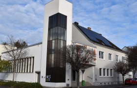 Moderne Kirche mit wei&szlig;er Fassade und Solarpanelen auf dem Dach.