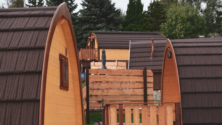 Several wooden glamping huts with brown roofs in a wooded area.