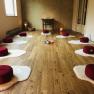 Meditation room with red cushions on white mats, candles and wooden floor.