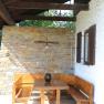 Wooden seating area under a covered area with a stone wall in the background.