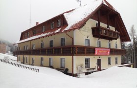 A large, snow-covered building with wooden cladding and balconies, surrounded by snow.
