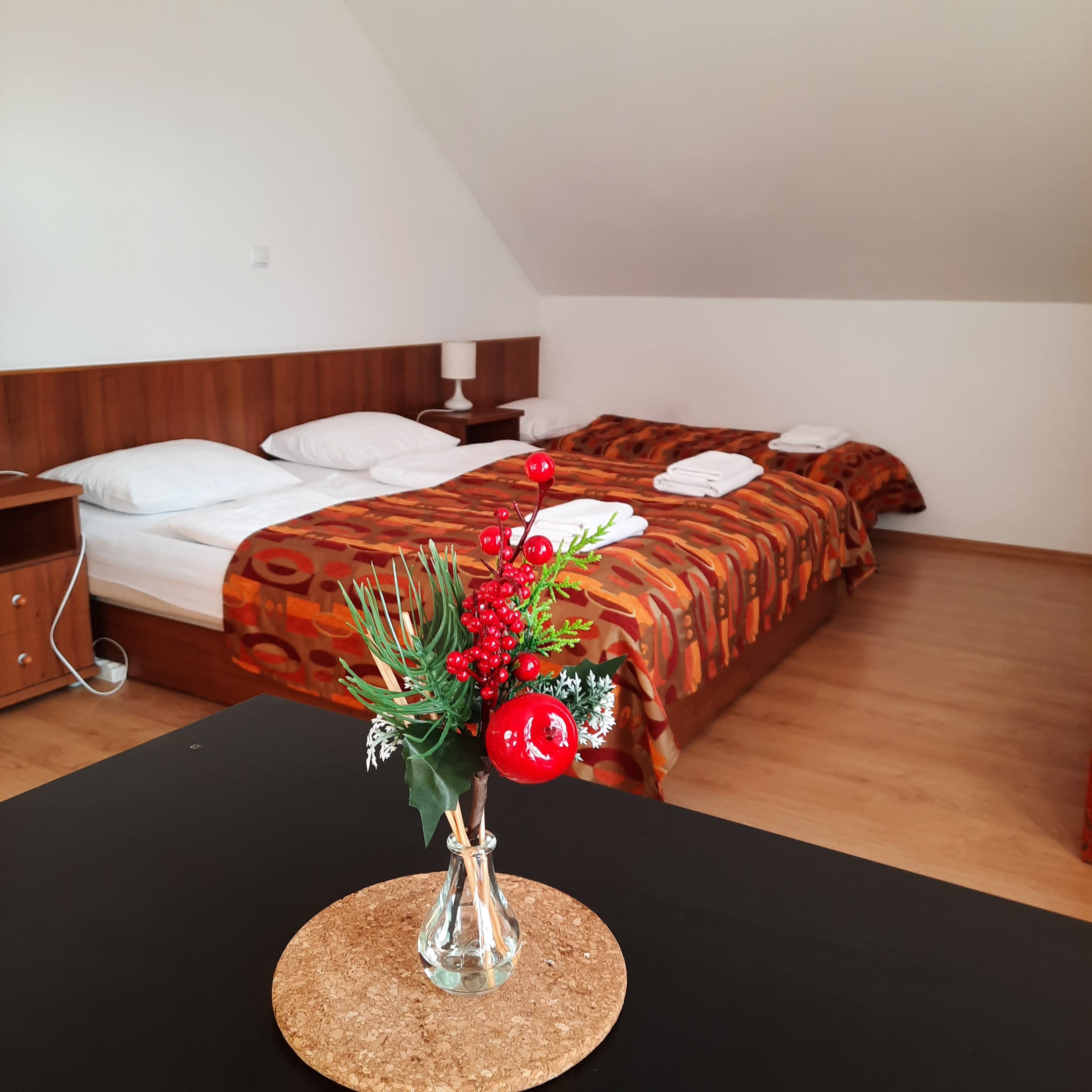Ein gemütliches Schlafzimmer mit zwei Betten, dekoriert mit roten Beeren in einer Vase im Vordergrund.