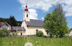 Kirche in Mitterbach mit rotem Turm und gr&uuml;nem Baum im Vordergrund.