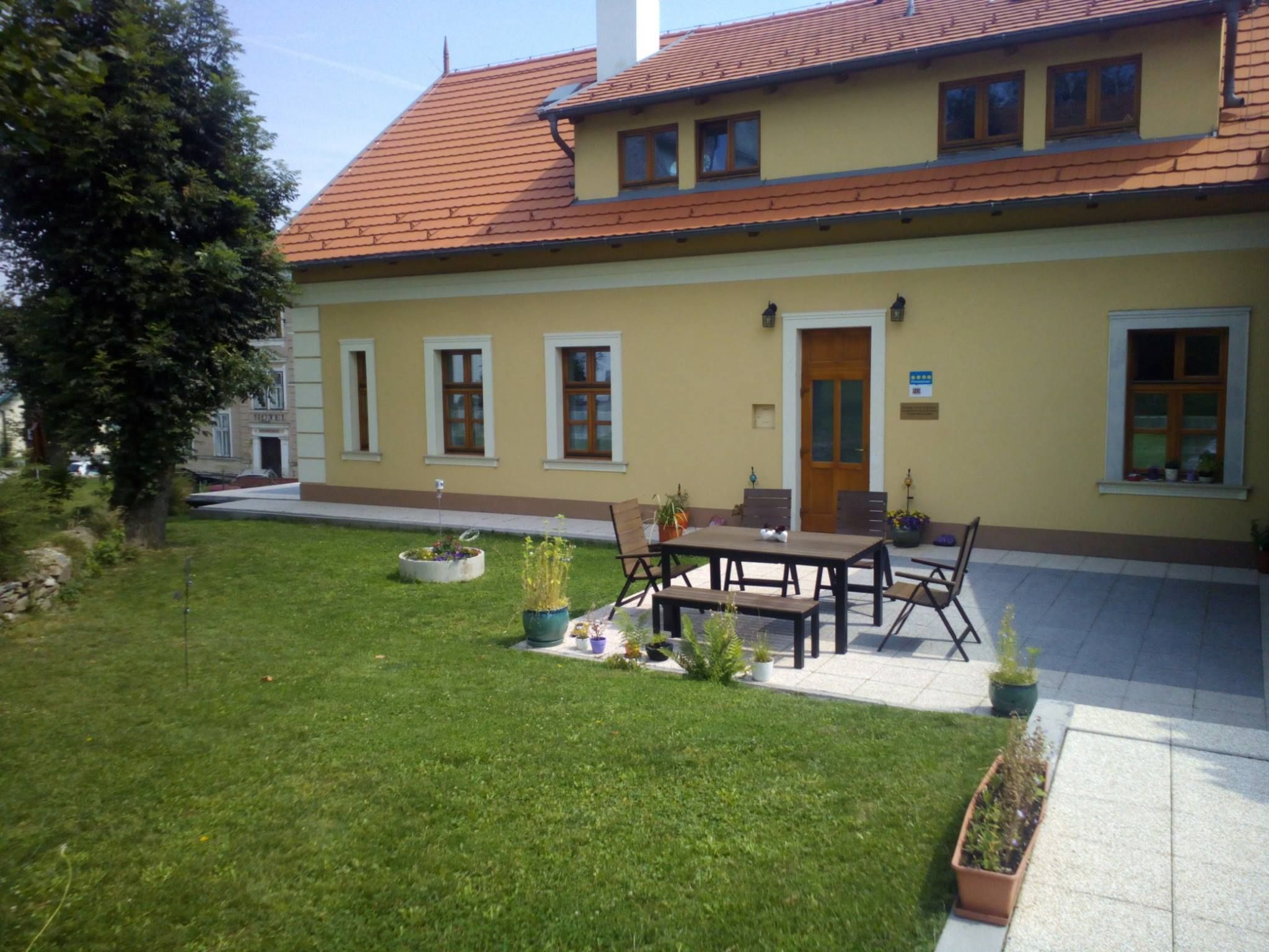 Ein gelbes Haus mit rotem Dach und Terrasse, umgeben von Rasen und Pflanzen.