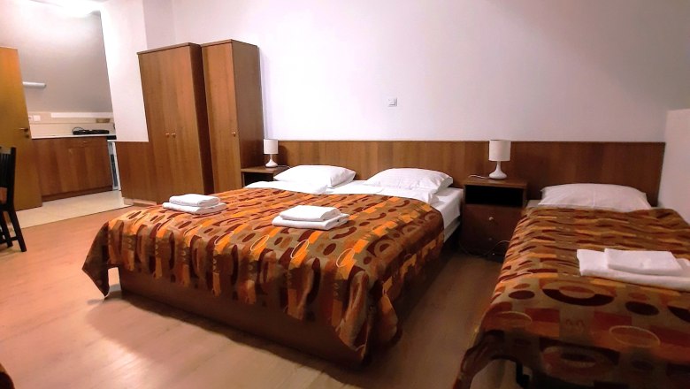 A triple room with two single beds and a double bed, all with patterned blankets. A closet and bedside tables are also provided.