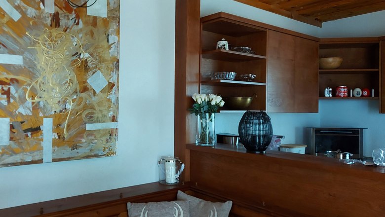 Wooden kitchen with artwork on the wall, vase with white roses and shelves with crockery.