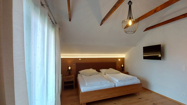 Double room with wooden beams, double bed, bedside tables, lamp and TV on the wall.