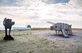 Spielplatz mit Holzspielger&auml;t in Form eines Tieres und Katzenskulptur.