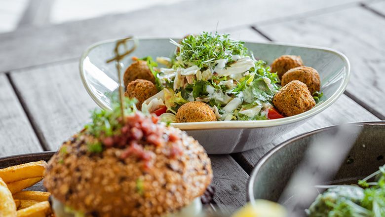 Ein tiefer Teller mit Salat und Falafel, im Vordergrund ein Burger.