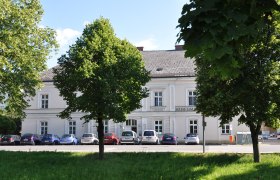 Ein wei&szlig;es Geb&auml;ude mit der Aufschrift 'Museum', umgeben von B&auml;umen und parkenden Autos.