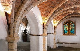 Gew&ouml;lbekeller mit Backsteinb&ouml;gen und buntem Glasfenster.