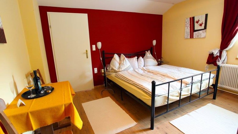 Cozy bedroom with double bed, table and chairs, yellow walls and red curtains.