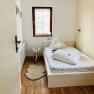 A small, cozy bedroom with a single bed, wooden floor and a small window with blinds.