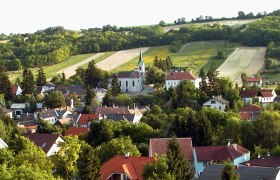 Landschaft mit Kirche und Dorf im Vordergrund, umgeben von Feldern und H&uuml;geln.