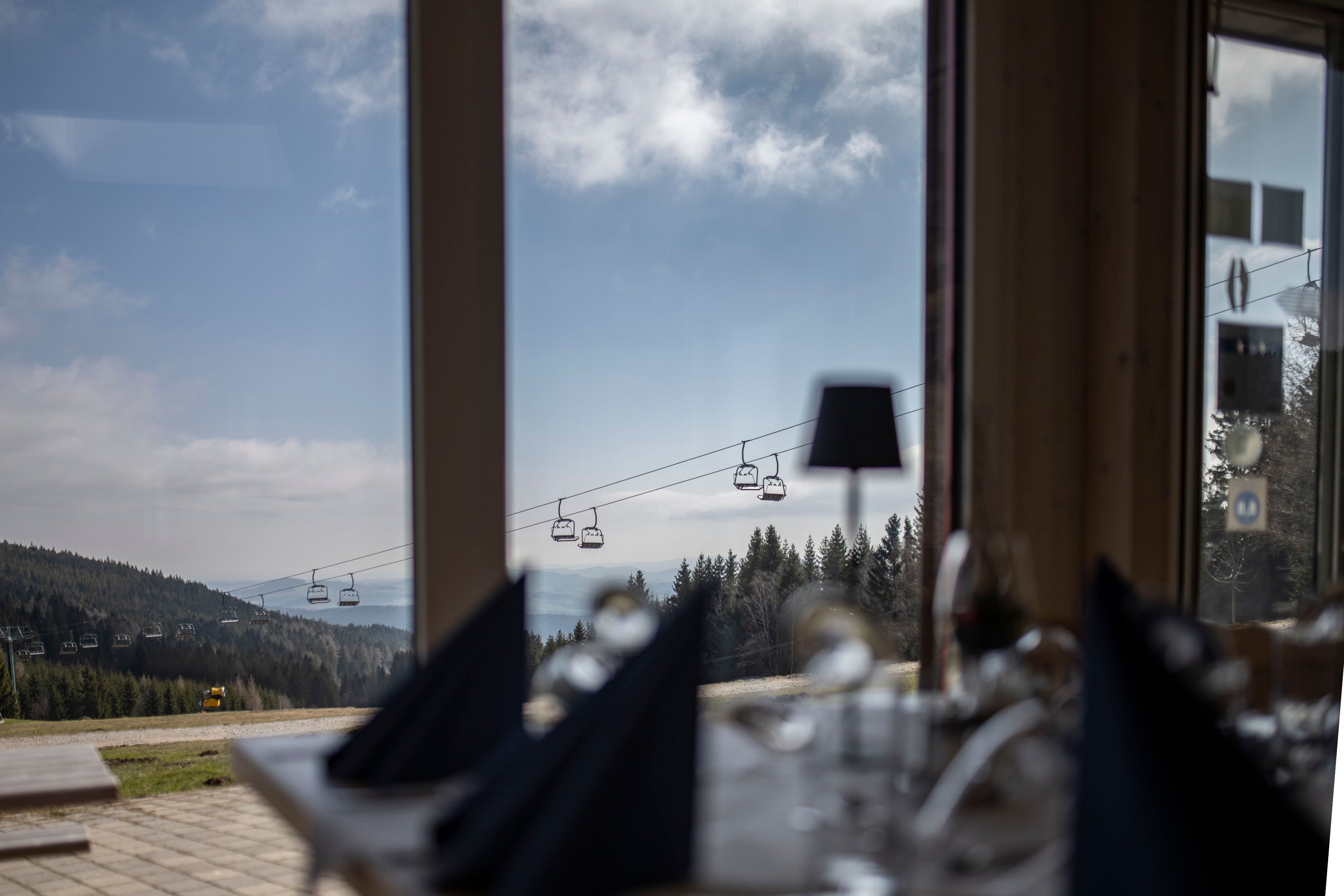Blick aus einem Fenster auf eine Berglandschaft mit Sessellift und Wald.