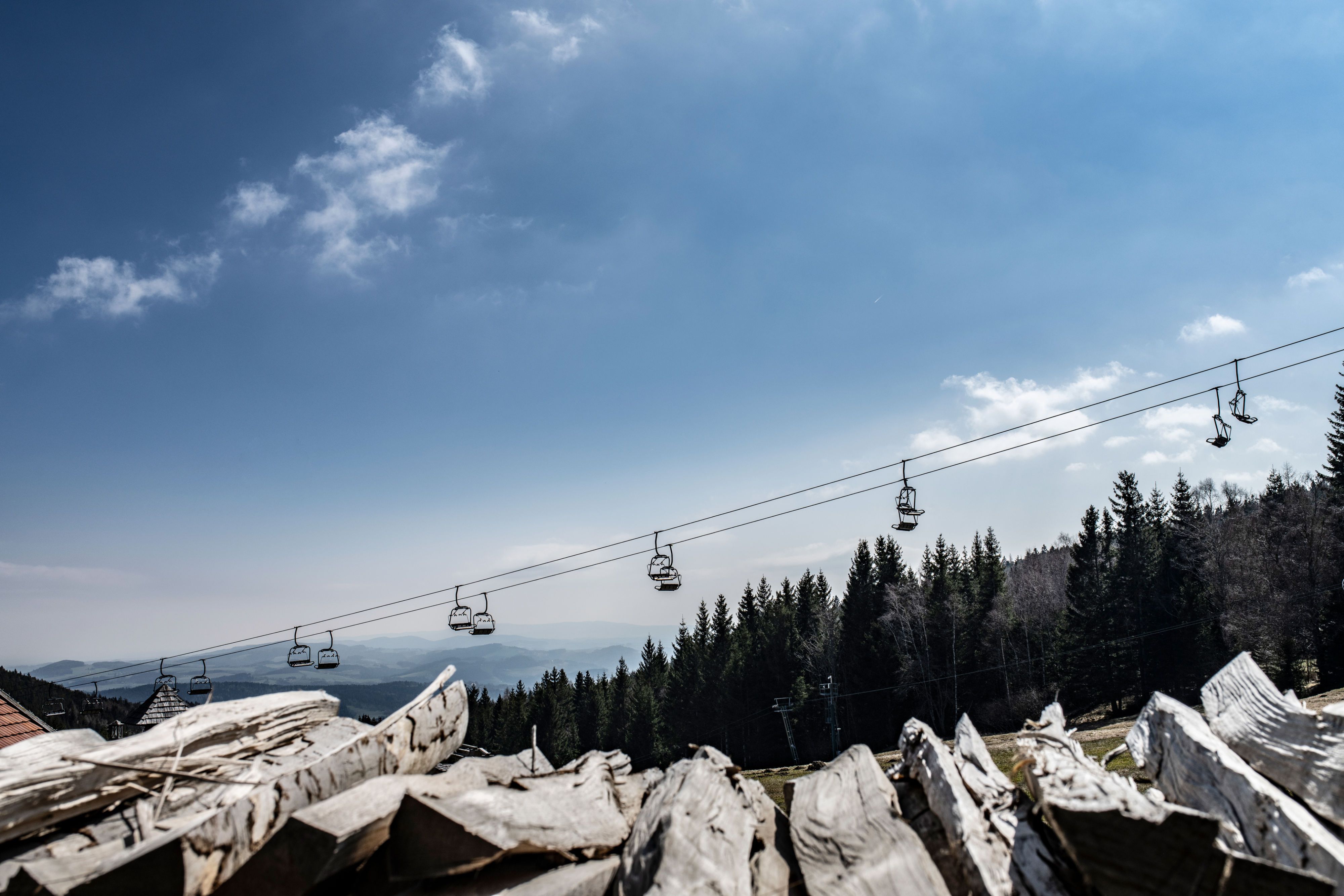 Blick auf eine Seilbahn über einem Wald mit blauem Himmel im Hintergrund.