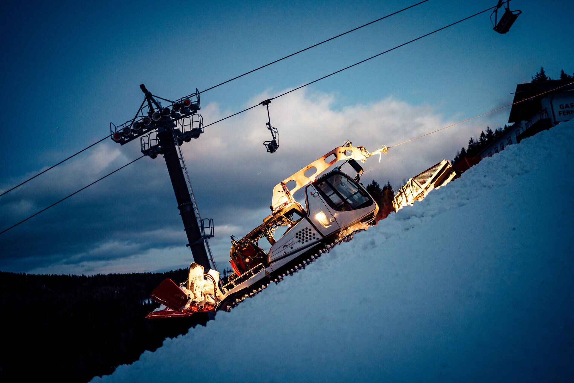 Die Pistenraupe gleitet sanft über die schneebedeckte Skipiste, während die Dämmerung die Landschaft in ein magisches Licht taucht. Die ruhige Atmosphäre und die schneebedeckten Hügel der Wiener Alpen laden zu einem unvergesslichen Winterabenteuer ein.