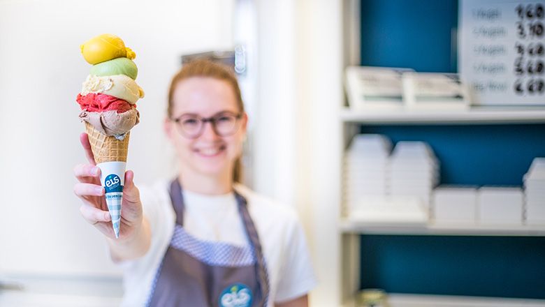 Eine lächelnde Frau hält eine Eistüte mit fünf verschiedenen Kugeln.