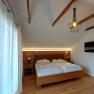 Double room with wooden beams, double bed, bedside tables, lamp and TV on the wall.