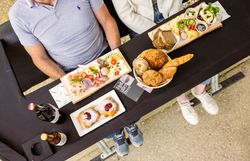 Von oben sieht man eine liebevoll und appetitlich arrangierte Jause auf dem Tisch eines Sessellifts. Verschiedene regionale Speisen und Getränke sind dekorativ angerichtet.