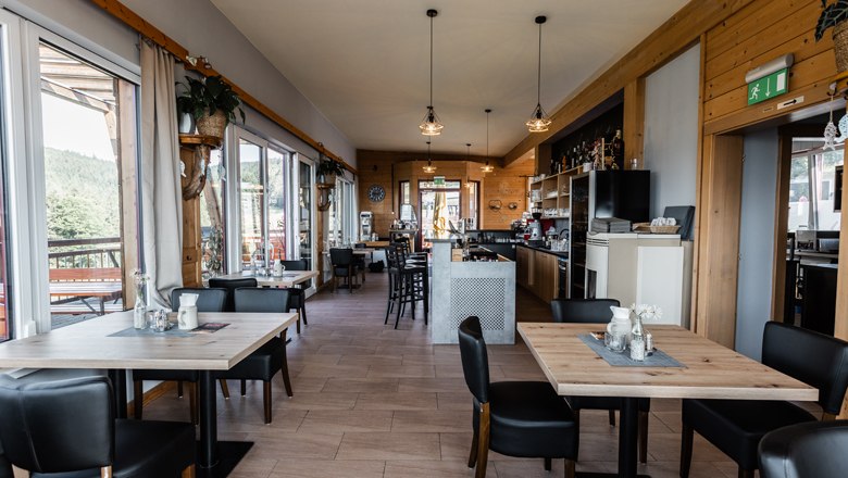 Innenansicht eines modernen Cafés mit Holzmöbeln und großen Fenstern.