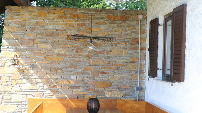 Wooden seating area under a covered area with a stone wall in the background.