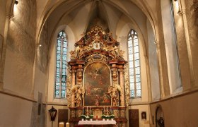 Innenansicht einer Kirche mit Altar und Buntglasfenstern.