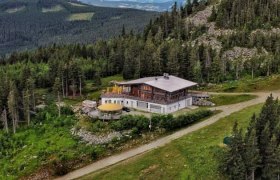 Aerial view of a mountain hut surrounded by forest and mountains.