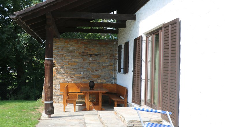 Terrace with lounger and wooden furniture next to a house with a shingle roof.