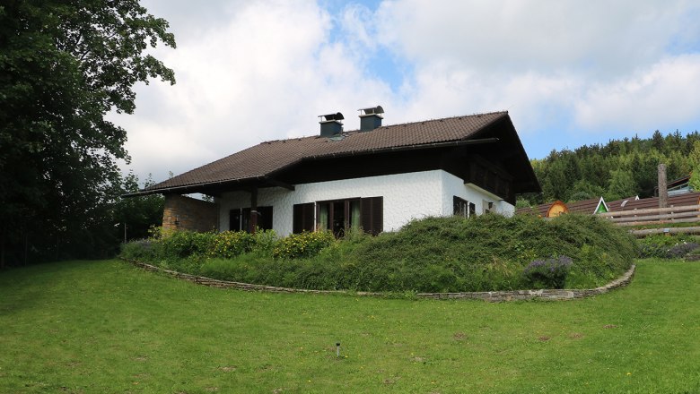 A white house with a brown roof in a green garden with trees and flowers.