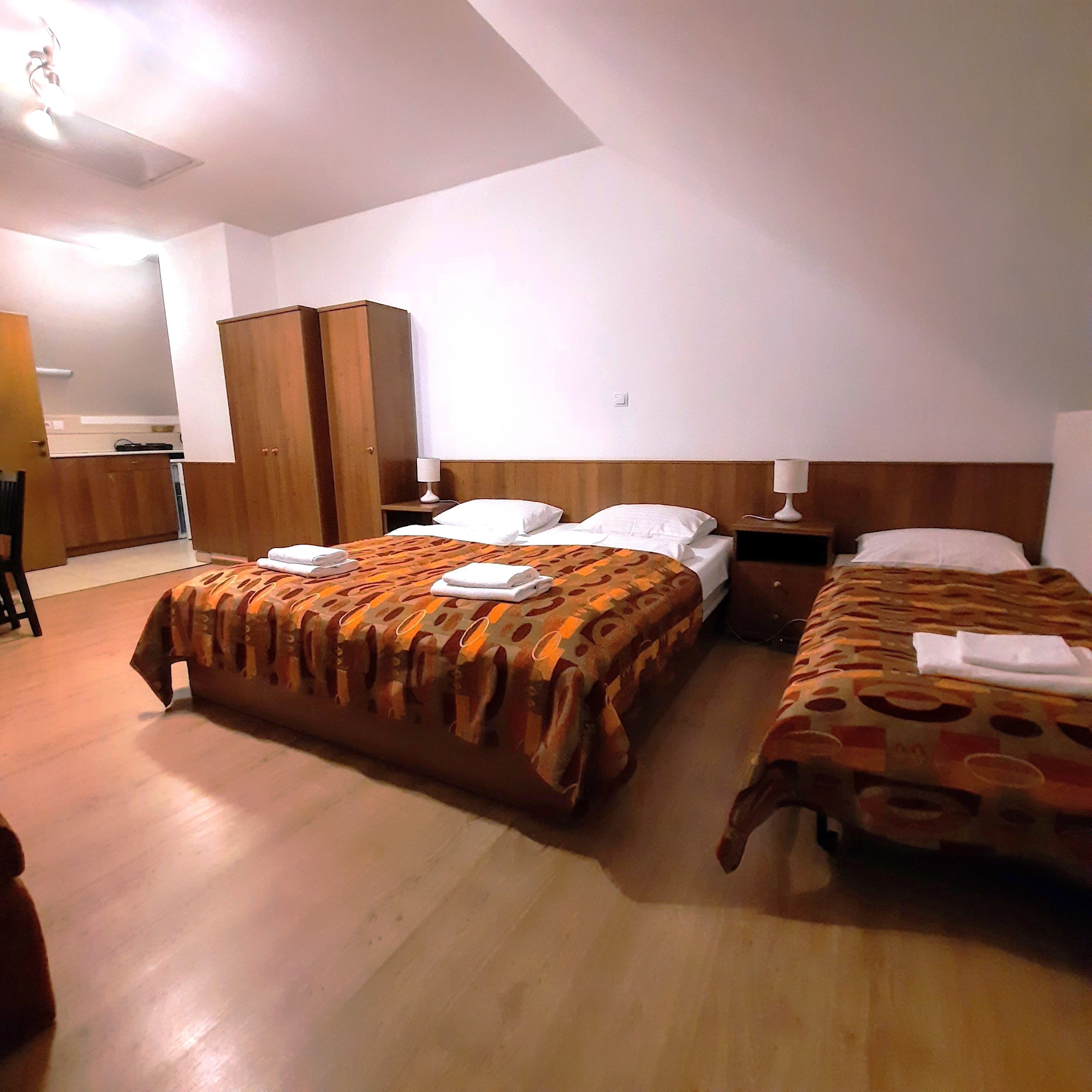 Ein Dreibettzimmer mit zwei Einzelbetten und einem Doppelbett, alle mit gemusterten Decken. Ein Kleiderschrank und Nachttische sind ebenfalls vorhanden.