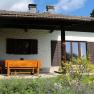 A house with a wooden seating area on the terrace, surrounded by a garden with flowers.