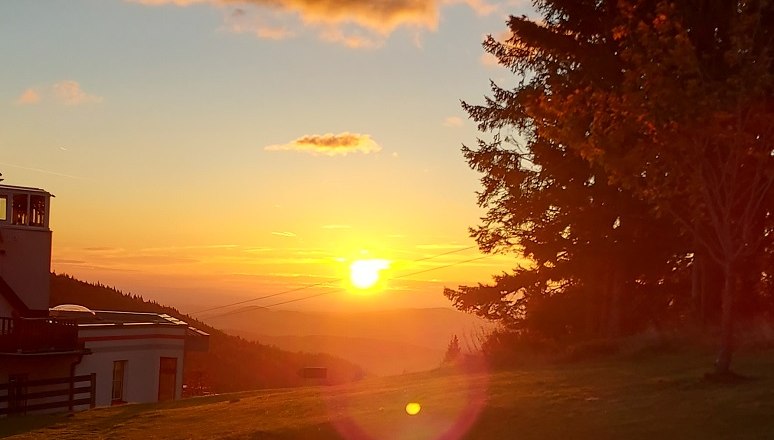 Naplemente egy r&eacute;t felett, fa asztallal &eacute;s paddal, a h&aacute;tt&eacute;rben f&aacute;k &eacute;s &eacute;p&uuml;letek.