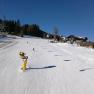 Skifahrer auf einer sonnigen Piste in Mönichkirchen mit Sessellift und Schneekanonen.