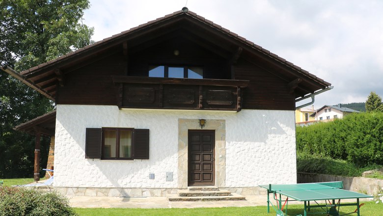 A white house with a wooden balcony and table tennis table in the garden.