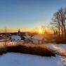 Winter landscape with sunrise over a snow-covered village and bare trees.