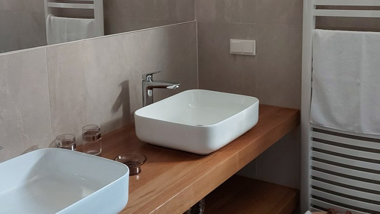 Modern bathroom with two white washbasins on a wooden top, towel rail and basket with towels.