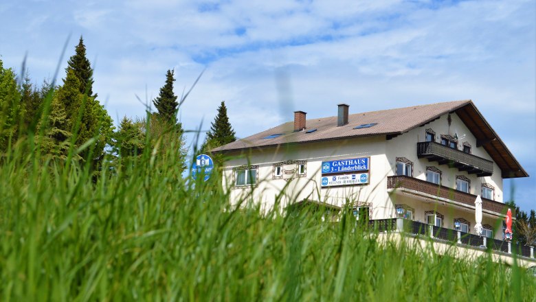 Gasthaus 3-L&auml;nderblick behind a meadow with trees in the background.