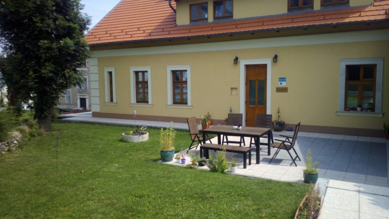 A yellow house with a red roof and terrace, surrounded by lawns and plants.