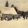 Historische Postkarte eines Skigebiets mit Menschen auf Skiern vor einer Hütte im Schnee.