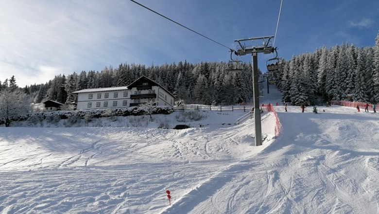 Direkt an der Skipiste, © Alpengasthof Fernblick, Fam. Pölzelbauer Schneebedeckte Skipiste mit Skilift und Wald im Hintergrund.